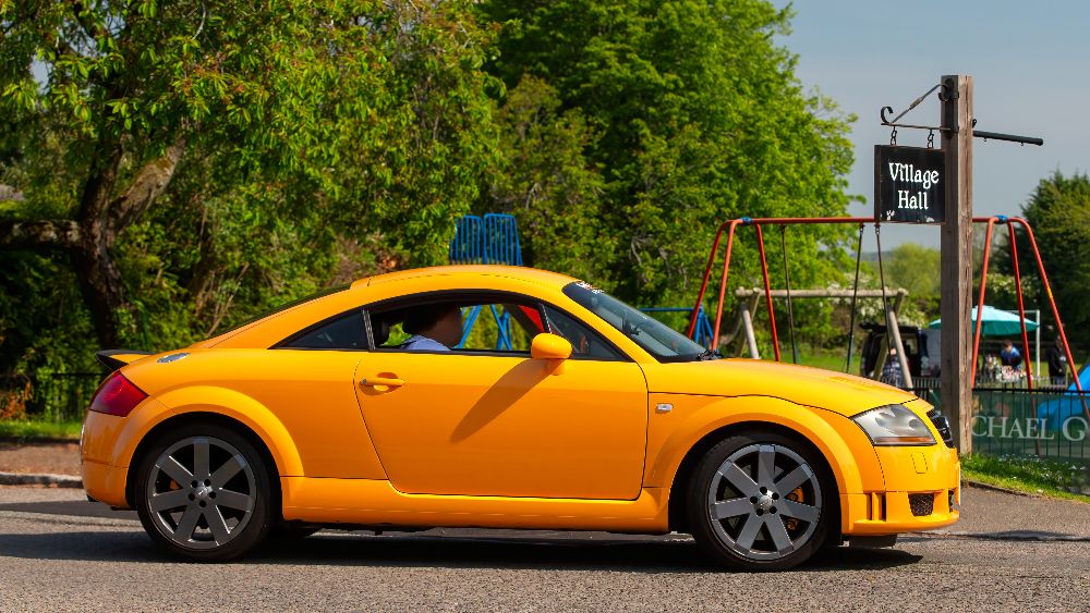 A bright orange modern classic Audi TT parked ouside a village hall